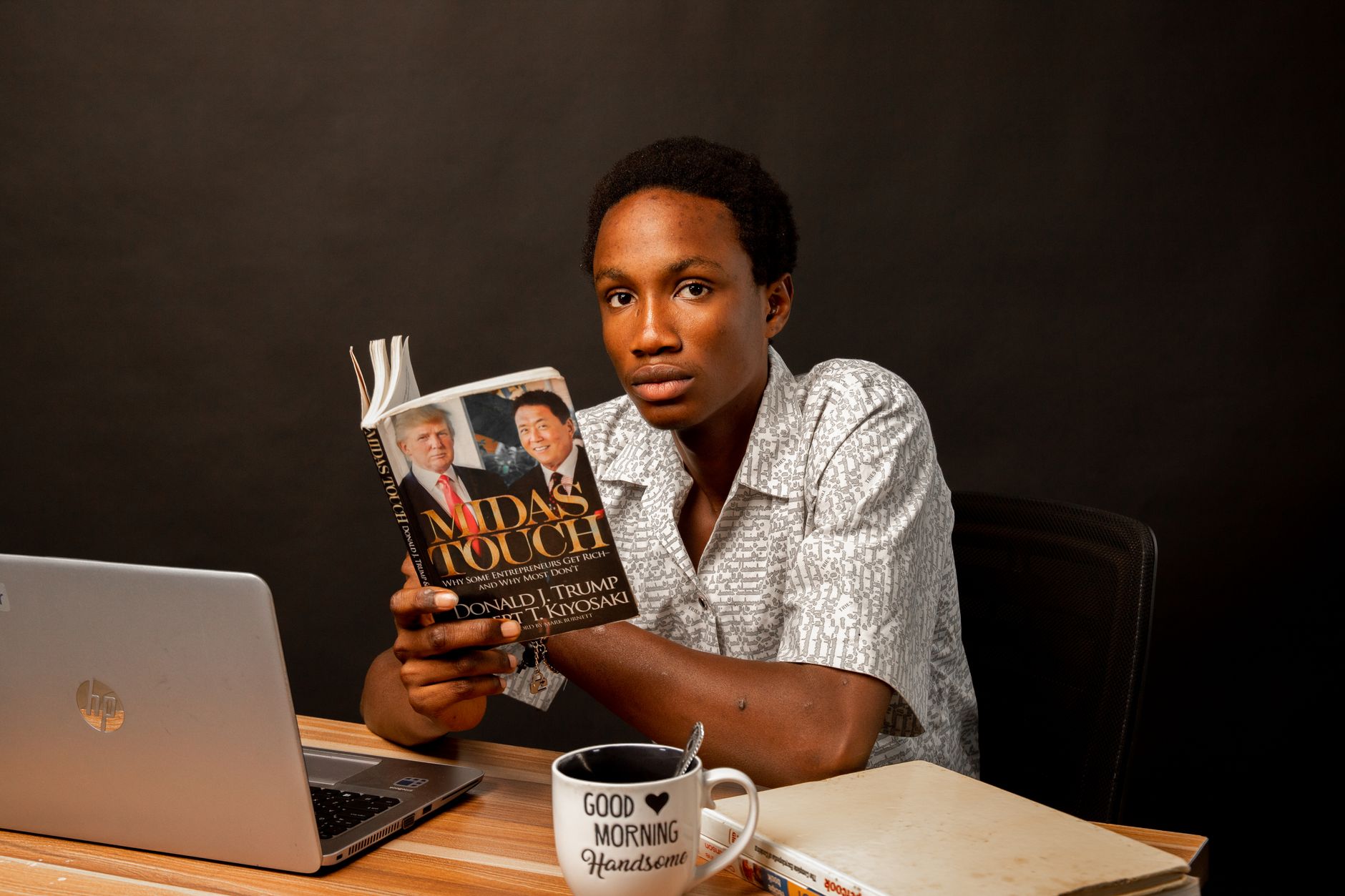 Reader with an open paperback book and laptop on a wooden desk