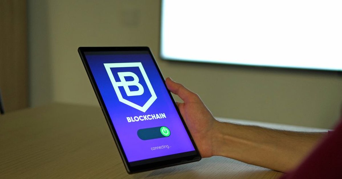 A hand holding a tablet with blockchain logo on screen, showcasing digital technology.
