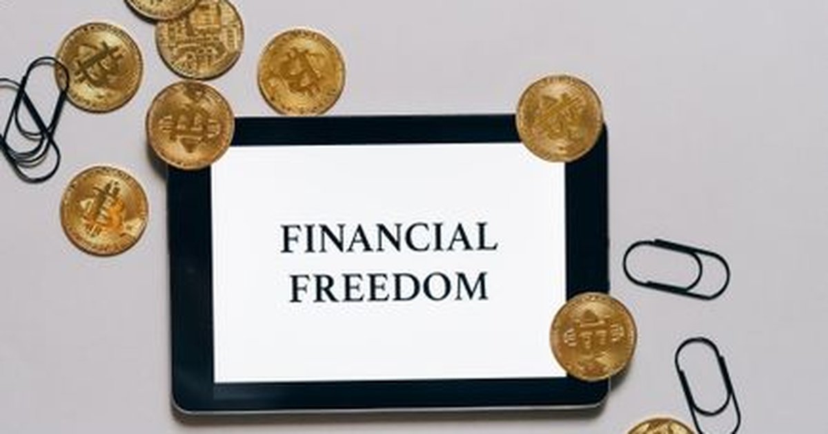 Top view of bitcoin coins and paper clips around a digital tablet displaying 'Financial Freedom'.
