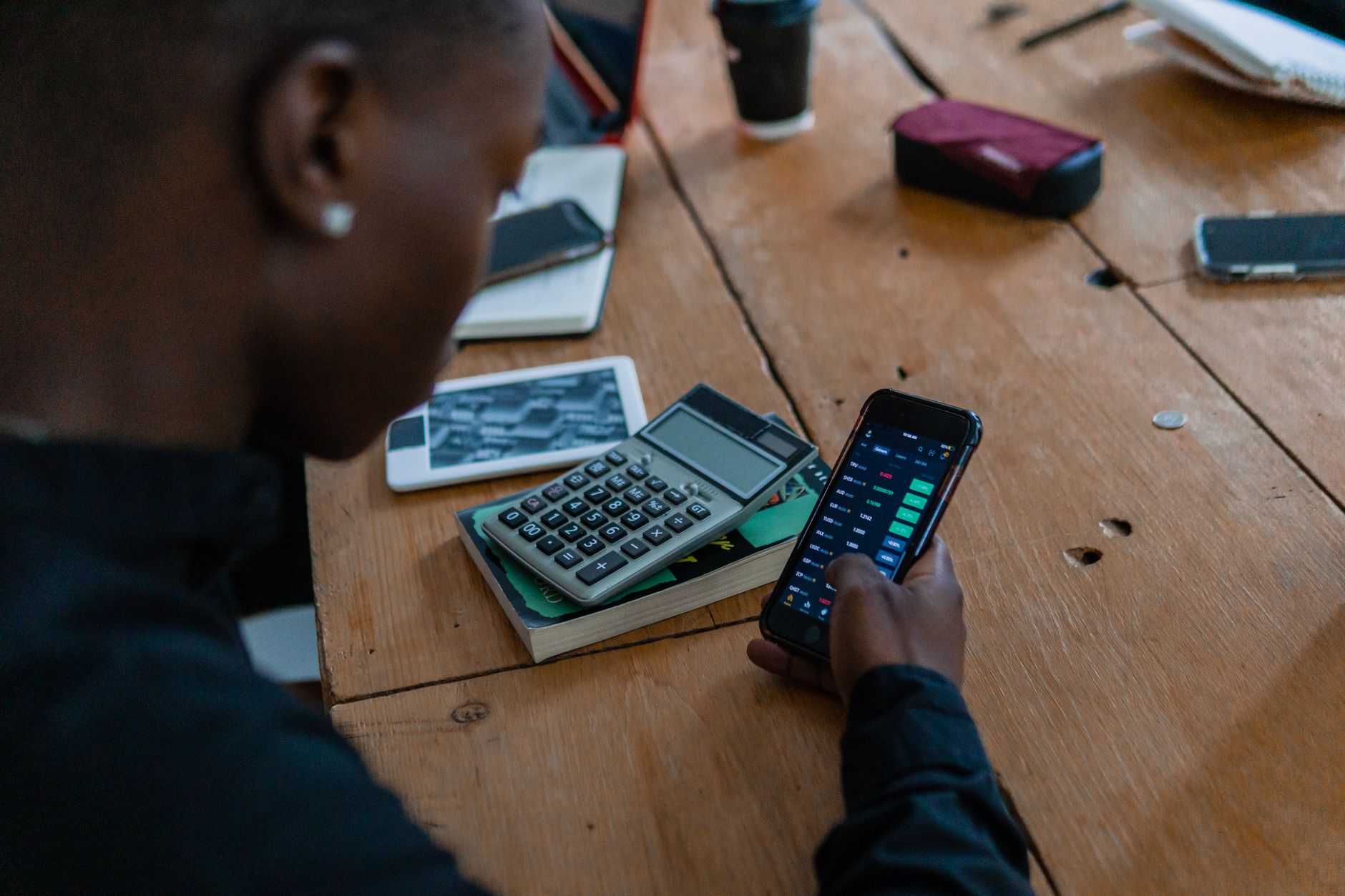 Hand holding a smartphone displaying a financial news feed above a wooden desk